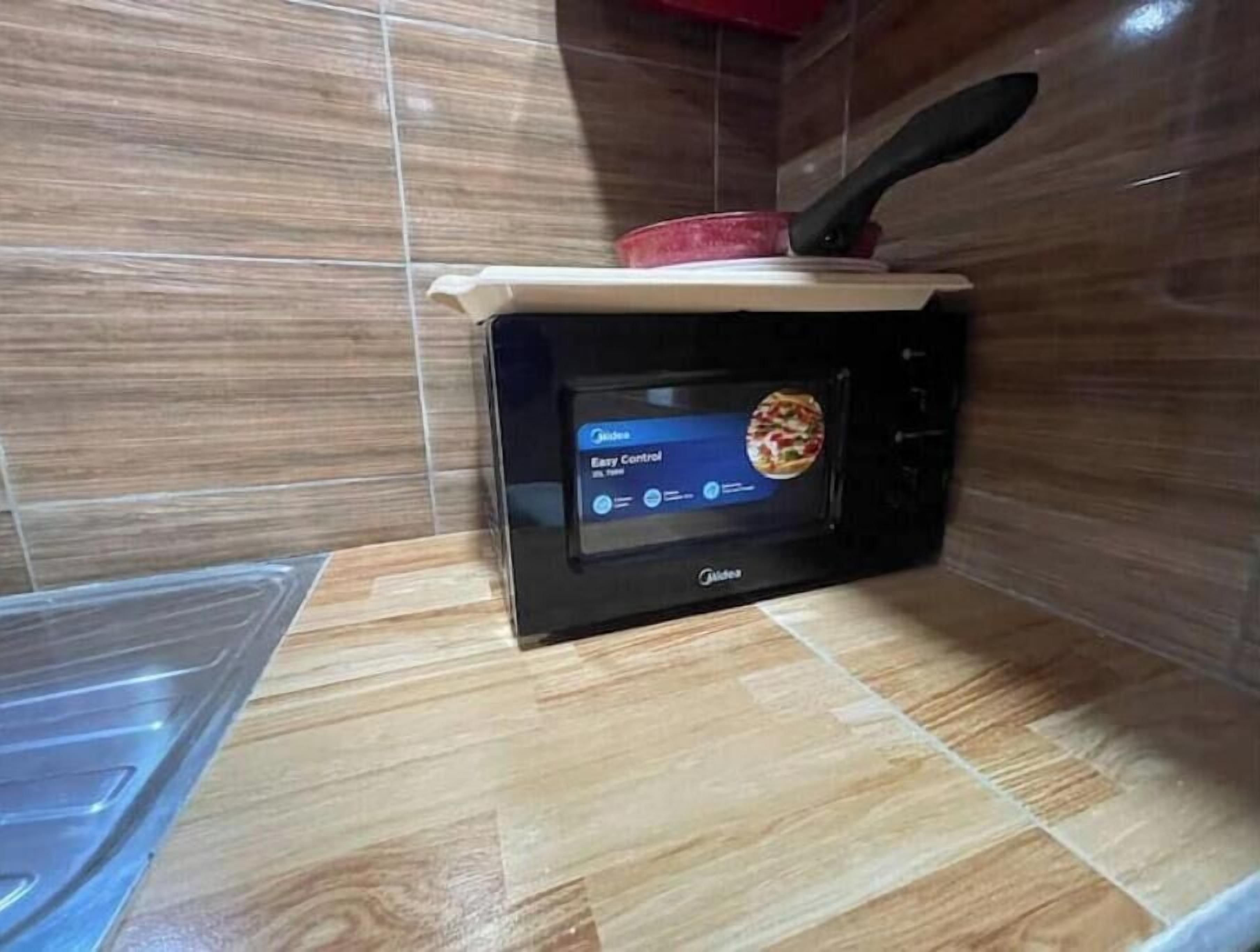 Een magnetron met een digitaal display, geplaatst op een houten aanrecht in een keuken met betegelde wanden.