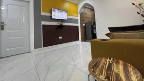 Un hall d’entrée moderne avec un sol en marbre, un comptoir d’accueil, un téléviseur et un espace détente agrémenté d’un fauteuil à motifs.