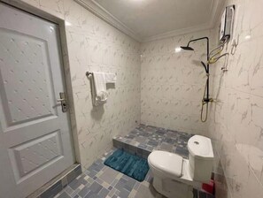 A bathroom with a toilet, a shower, and a tiled floor.