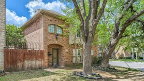 A two-story brick house with a front door, windows, and a large tree in the front yard. - Holland Heights (Dallas)