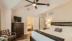 A bedroom with a bed, a dresser, a TV, a chair, and a ceiling fan. - Holland Heights (Dallas)