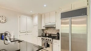 A kitchen with white cabinets, a stainless steel refrigerator, a stove, and a clock on the wall. - Holland Heights (Dallas)
