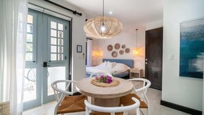 Ein modernes Zimmer mit einem Bett, einem Esstisch mit Stühlen und einem großen Fenster mit Vorhängen.