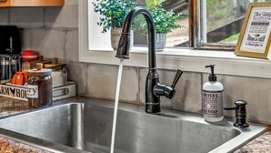 Un lavamanos de cocina con un grifo moderno, un dispensador de jabón y una ventana con una planta en maceta.