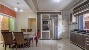 A modern kitchen with built-in appliances, a dining area with wooden chairs, and a chandelier.