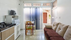 A modern kitchen with a stove, microwave, and coffee maker. There is a dining area with a table and chairs. A brown sofa is in the living area.