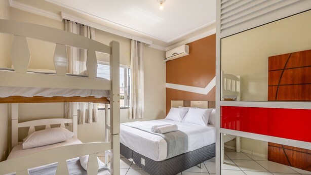 A hotel room with bunk beds, a single bed, an air conditioning unit, a mirror, and a red accent wall.