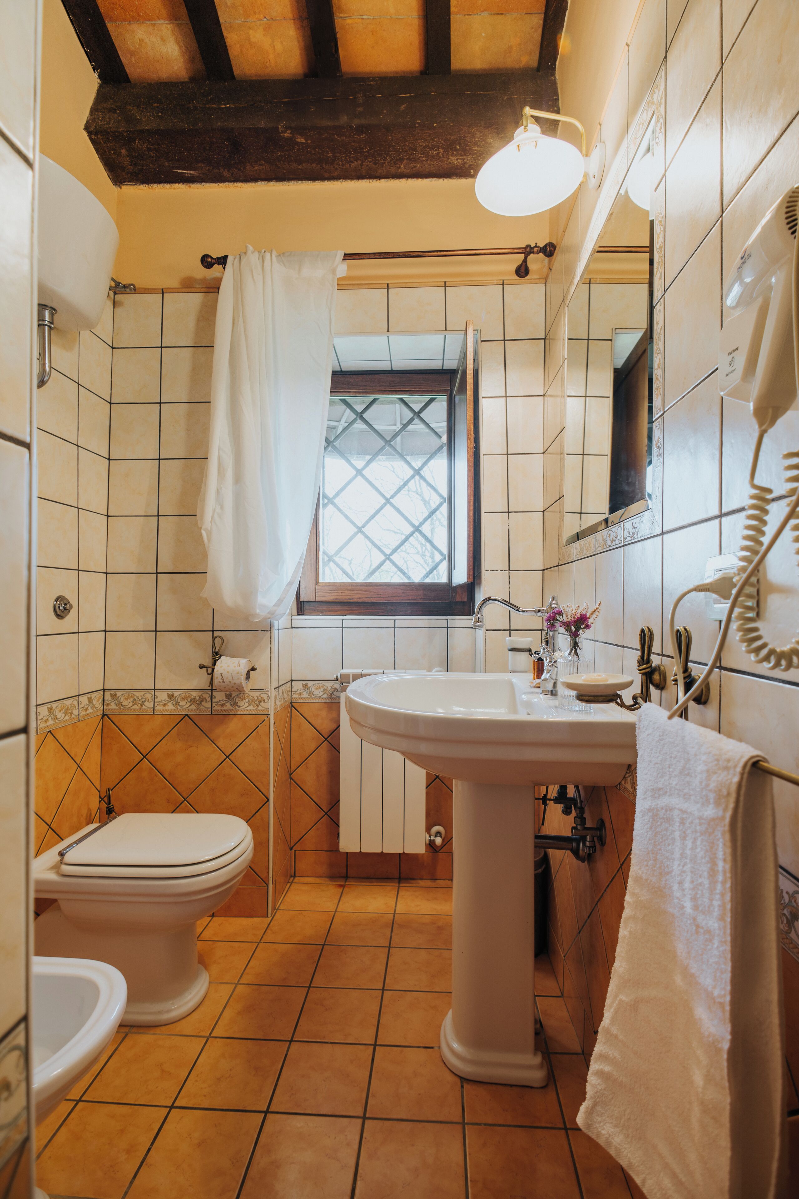 Un baño con lavamanos blanco, inodoro y ventana con cortina.