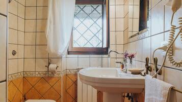 Un baño con lavamanos blanco, inodoro y ventana con cortina.