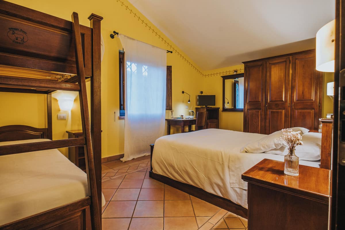 Ein Hotelzimmer mit einem hölzernen Bett, einem separaten Holzstuhl, einem Nachttisch mit Lampe sowie einem kleinen Tisch mit einer Vase.