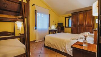 A hotel room with a wooden bed, a separate wooden chair, a bedside table with a lamp, and a small table with a vase.