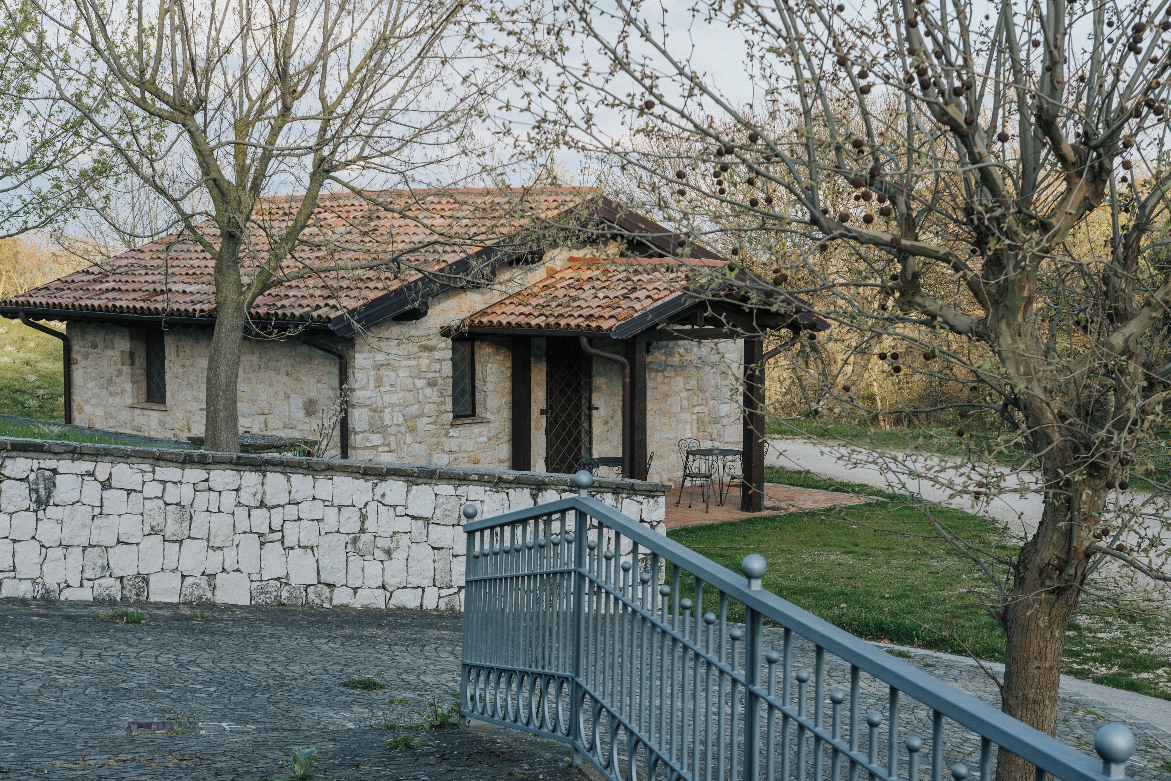 A stone building with a tiled roof, a metal railing, and a tree in the foreground.