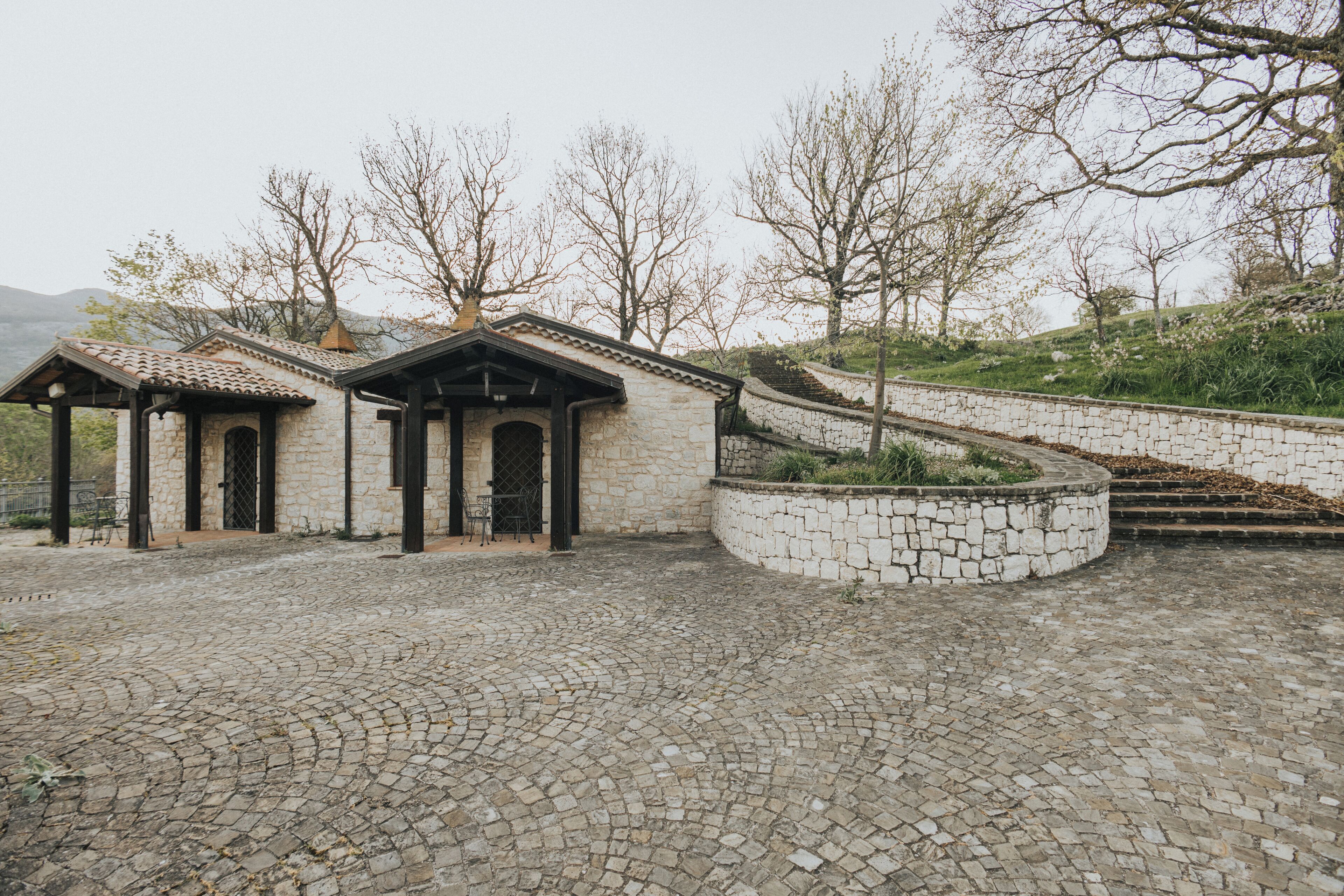A stone building with a tiled roof, a stone staircase, and a cobblestone courtyard.