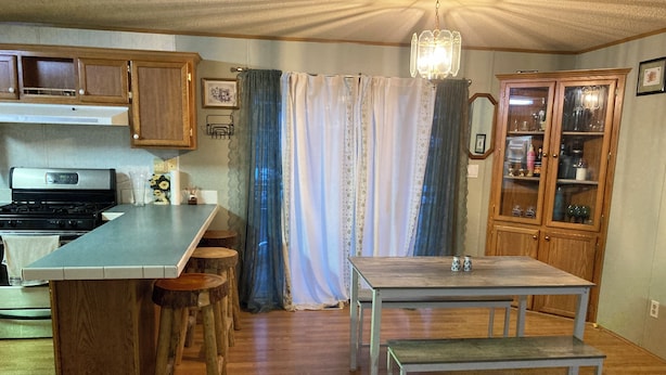 A compact kitchen with a central island, wooden bar stools, a dining table with benches, and a cabinet with glass doors.