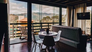 A room with a large window, a sofa, a dining table with chairs, and a flat-screen TV. - Loft Felicidade  (Urubici)