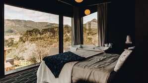 A bedroom with a large window, a bed, a bathtub, and a view of a mountainous landscape. - Loft Felicidade  (Urubici)