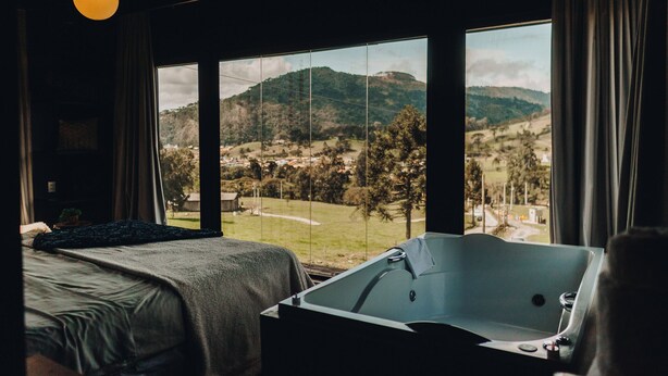 A bedroom with a large window, a bathtub, and a bed. - Loft Felicidade  (Urubici)