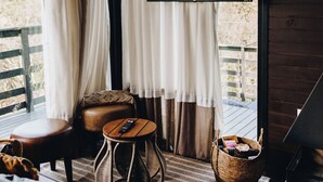 A cozy room with a large window, a flat-screen TV, a sofa, a small round table, and a wicker basket. - Loft Felicidade  (Urubici)