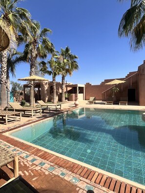 A pool area with lounge chairs, palm trees, and a thatched-roof structure. - villa 4 chambres climatisée avec piscine privée sans vis à vis à Marrakech (Marrakesh)