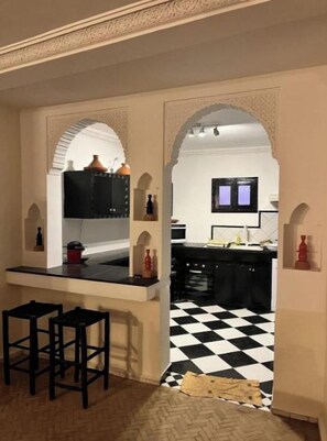 Une cuisine avec des meubles de couleur noire, un plan de travail noir et un sol à carreaux. On y trouve deux tabourets noirs près du plan de travail.