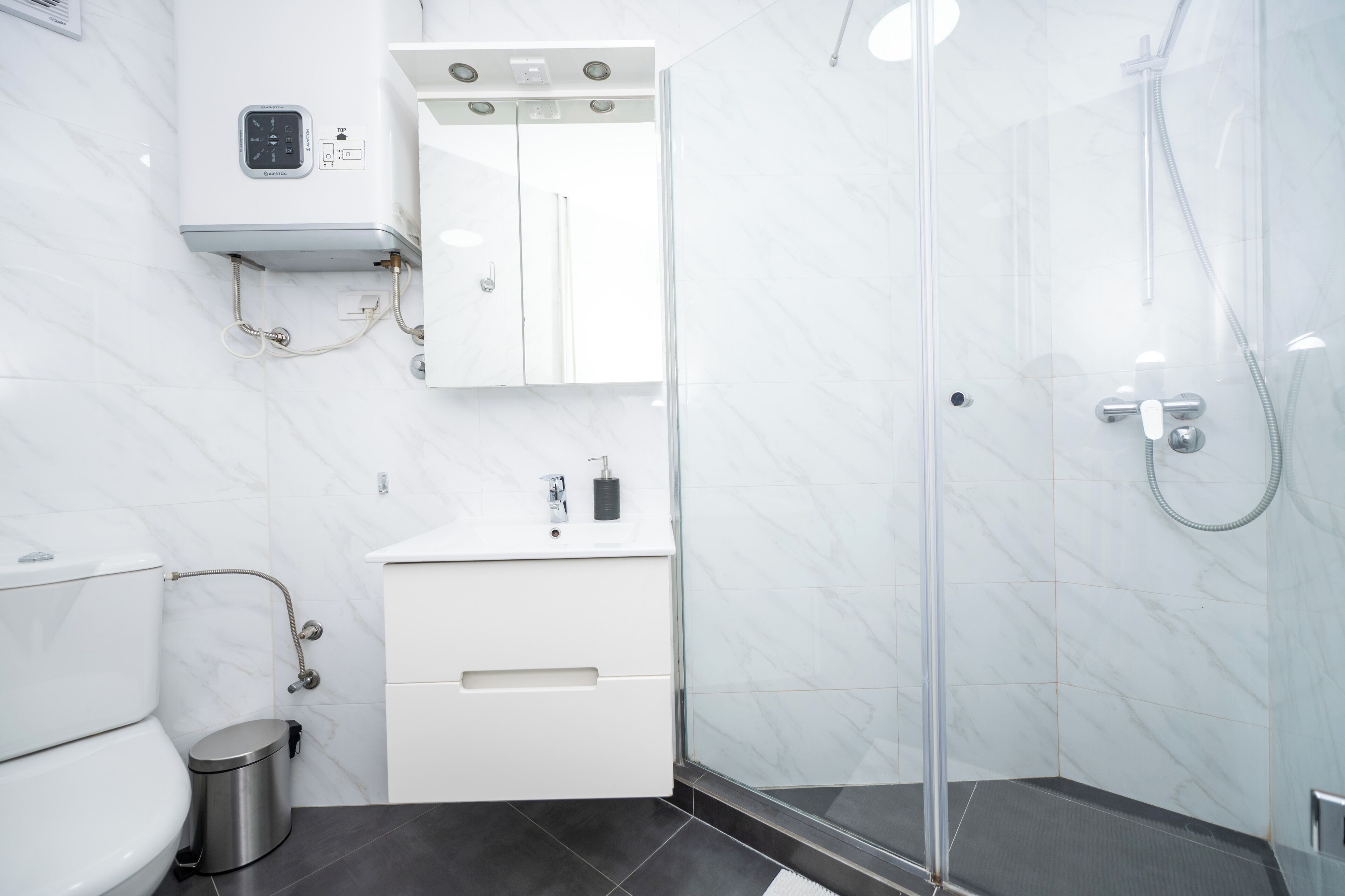 Un baño moderno con cabina de ducha de vidrio, inodoro, lavabo con dispensador de jabón y espejo sobre el mueble de baño.