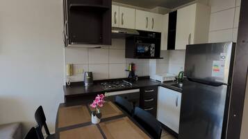 Una cocina moderna con armarios blancos, un refrigerador negro y un microondas. Hay una mesa de comedor con sillas y un florero con flores.