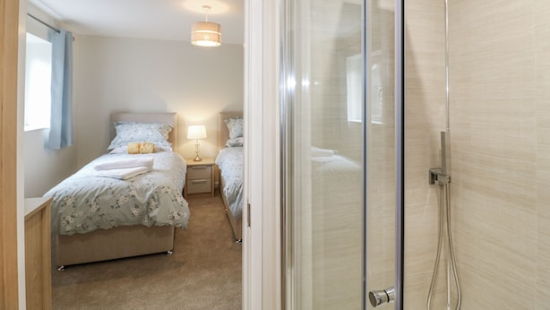 Een hotelkamer met twee bedden, een nachtkastje met lamp, een douchegedeelte en een raam met gordijnen.