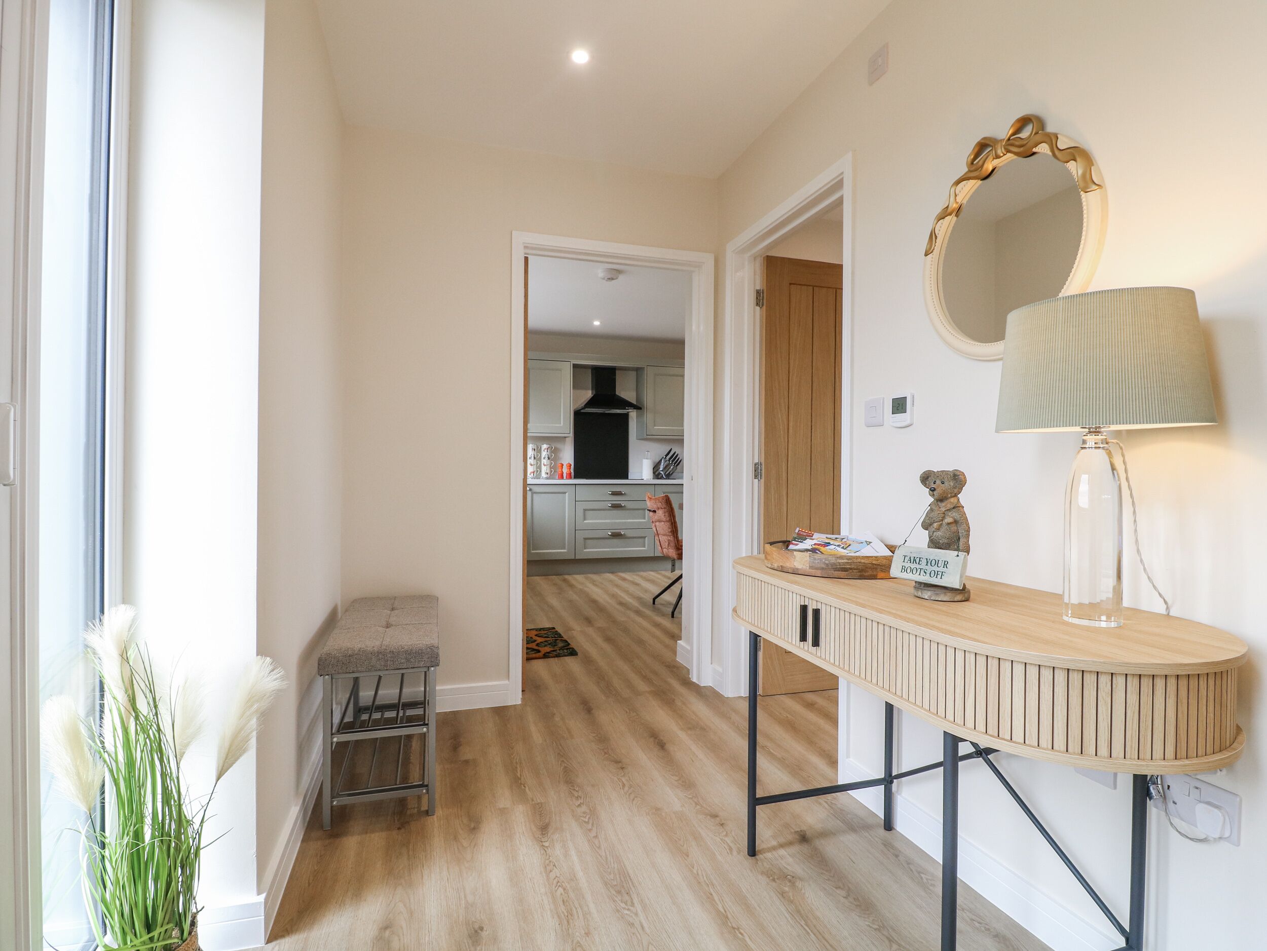 A hallway leading to a kitchen with a wooden bench, a mirror, and a lamp.