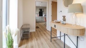 Een gang die uitkomt bij een keuken met een houten bank, een spiegel en een lamp.
