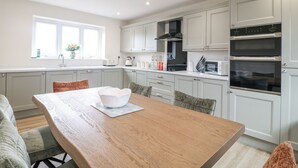 Een moderne keuken met witte kastjes, een dubbele oven en een eethoek met een houten tafel en stoelen.