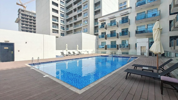 A swimming pool with lounge chairs and umbrellas, surrounded by a high-rise building with balconies. - JVC Studio for 2 People With Pool (Dubai)