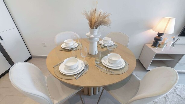 A round dining table set with white plates, bowls, and cutlery, surrounded by white chairs. - Dubai Hills for 4 People in a Great Location (Dubai)
