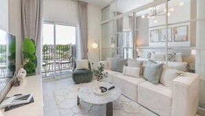 A modern living room with a sofa, a coffee table, and a balcony with a view. - Dubai Hills for 4 People in a Great Location (Dubai)