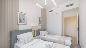A hotel room with two beds, a nightstand with a lamp, and artwork on the walls. - Dubai Hills for 4 People in a Great Location (Dubai)