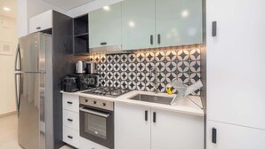 A modern kitchen with a stainless steel refrigerator, a built-in oven, a gas stove, and a coffee maker. - Dubai Hills for 4 People in a Great Location (Dubai)