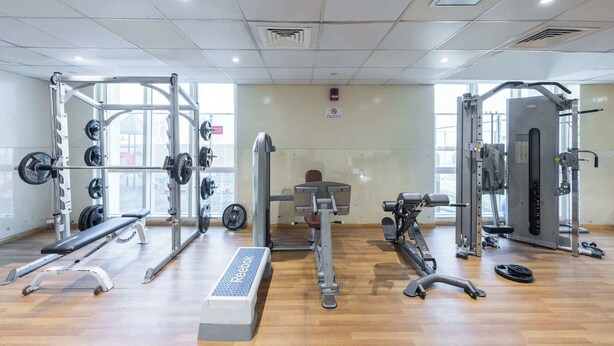 A gym with various exercise equipment, including a bench press, squat rack, and weight machines. - Production City Sleeps 4 With Water Views (Dubai)