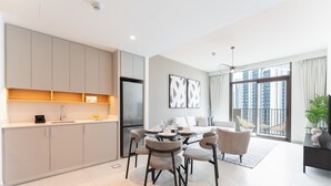 Eine moderne Küche mit grauen Schränken und einem eingebauten Kühlschrank. Es gibt eine Essecke mit einem Glastisch und vier Stühlen. Das Zimmer verfügt über große Fenster mit Blick auf hohe Gebäude.