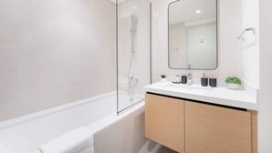 Ein modernes Badezimmer mit einer gläsernen Duschkabine, einem weißen Waschbecken inklusive Spiegel und Holzschränken.