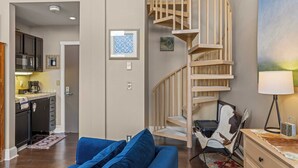 A modern living room with a blue sofa, a wooden spiral staircase, and a kitchen area visible through an open door. - Blue Mesa Lodge 40A by Avantstay Ski In/ Ski Out Unit w/ Balcony! (Telluride)