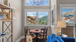 A dining area with a table, chairs, a chandelier, and a view of a mountain landscape through a window. - Blue Mesa Lodge 40A by Avantstay Ski In/ Ski Out Unit w/ Balcony! (Telluride)