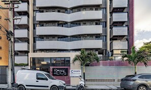 Un edificio a più piani con facciata piastrellata, un furgone bianco parcheggiato e uno scooter sul marciapiede.