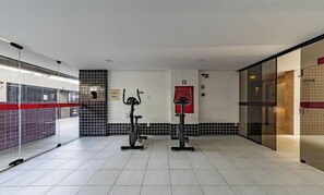 Una palestra con due cyclette, pavimento piastrellato e parete di vetro con un cartello rosso.