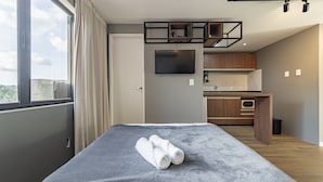 Una habitación de hotel moderna con una cama grande, un televisor de pantalla plana, una kitchenette y vistas a la ciudad.