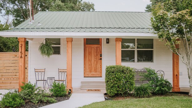 A single-story house with a green metal roof, a wooden front door, and a small porch with two chairs and a table. - 2BR/1BA in Golf Cart District near Beaches and Downtown! The Beachcomber A (Ocean Springs)