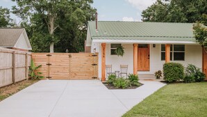 A house with a green metal roof, a wooden gate, and a small patio with two chairs and a table. - 2BR/1BA in Golf Cart District near Beaches and Downtown! The Beachcomber A (Ocean Springs)