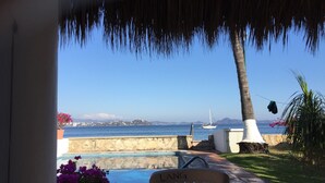 A pool area with a chair labeled "LANG" and a view of the sea with a sailboat. - Casa Lang 4 BR/Bath pool on flat calm beach steps to restaurants in secure area. (Manzanillo)