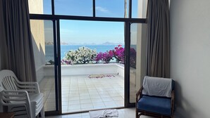 A room with a balcony, white plastic chairs, a wooden chair with a blue cushion, and a bed with a patterned blanket. - Casa Lang 4 BR/Bath pool on flat calm beach steps to restaurants in secure area. (Manzanillo)