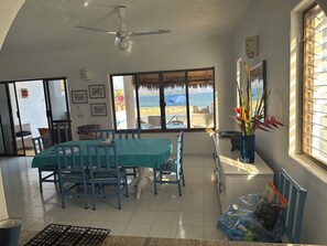 A dining area with a table set for four, a ceiling fan, and a view of the sea through large windows.