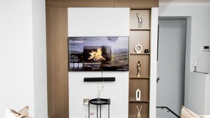 A modern living room with a flat-screen TV mounted on the wall, a small side table with a vase, and a built-in shelf with decorative items.