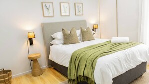 A neatly arranged bedroom with a bed, bedside lamps, a small round table, and a basket.